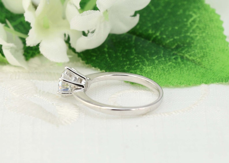 May include: A silver ring with a single, round, clear gemstone set in a prong setting.