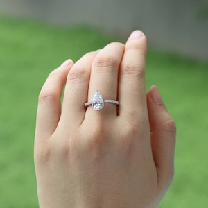 May include: A pear-shaped diamond engagement ring with a pave setting. The ring is set in a silver band.