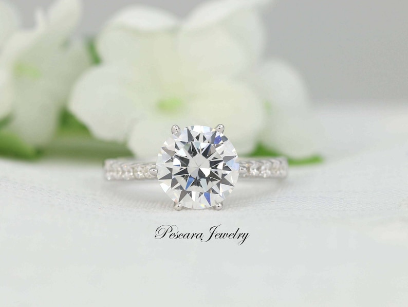 May include: A silver engagement ring with a large, round, clear diamond center stone and a band of smaller diamonds.
