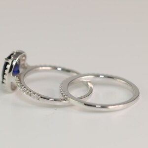 May include: A set of two silver rings with a blue gemstone in the center of the larger ring. The larger ring has a halo of smaller gemstones around the center stone. The smaller ring has a band of smaller gemstones.