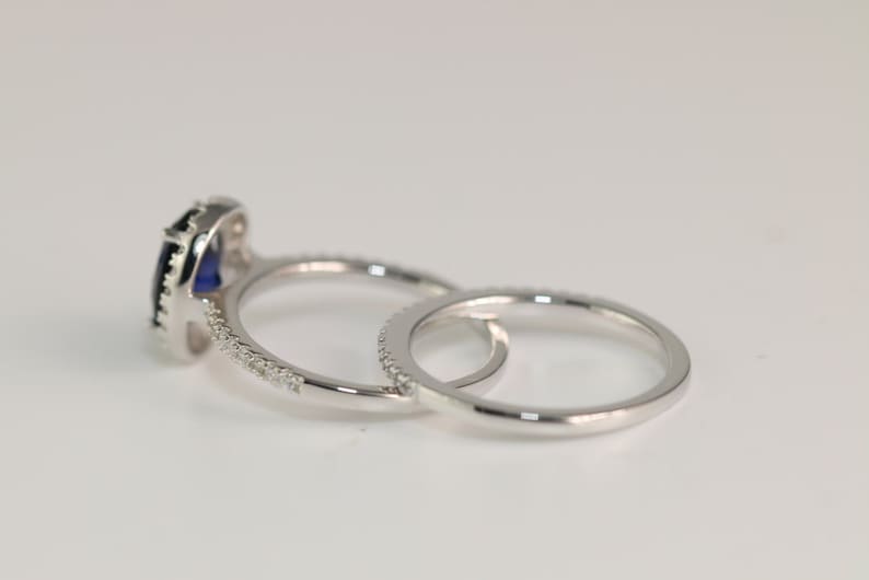 May include: A set of two silver rings with a blue gemstone in the center of the larger ring. The larger ring has a halo of smaller gemstones around the center stone. The smaller ring has a band of smaller gemstones.