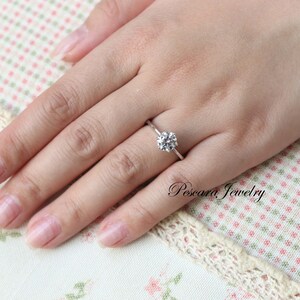 May include: A silver ring with a round, clear gemstone on a finger.