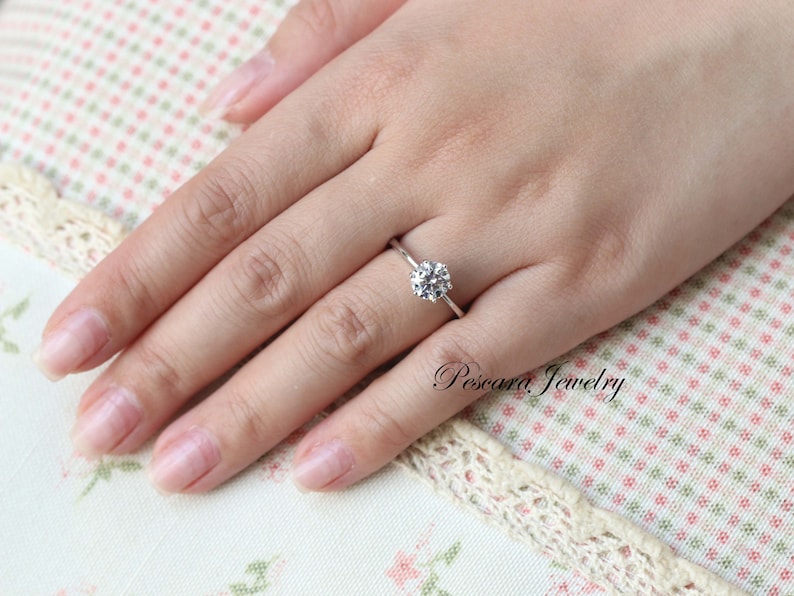 May include: A silver ring with a round, clear gemstone on a finger.