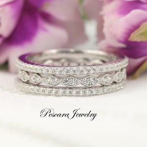 Peut inclure: Une bague en argent à trois bandes avec une rangée de petits diamants ronds et une rangée de diamants ovales plus grands. La bague est posée sur un fond blanc.