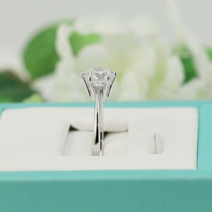 May include: A silver ring with a large, clear, round gemstone in a prong setting. The ring is in a light blue ring box.