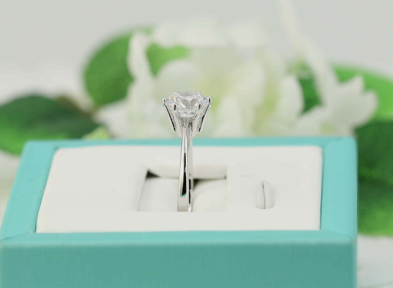 May include: A silver ring with a large, clear, round gemstone in a prong setting. The ring is in a light blue ring box.