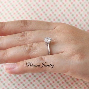 May include: A silver ring with a large, clear, round gemstone set in a prong setting. The ring is on a person's finger.