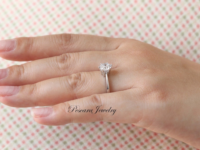 May include: A silver ring with a large, clear, round gemstone set in a prong setting. The ring is on a person's finger.