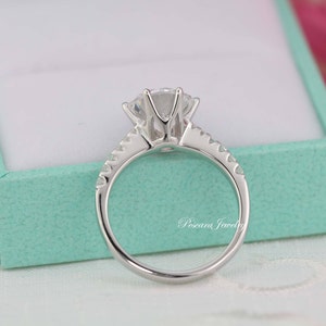 May include: A silver ring with a large, clear, round gemstone in the center. The ring has a band of smaller gemstones around the center stone.