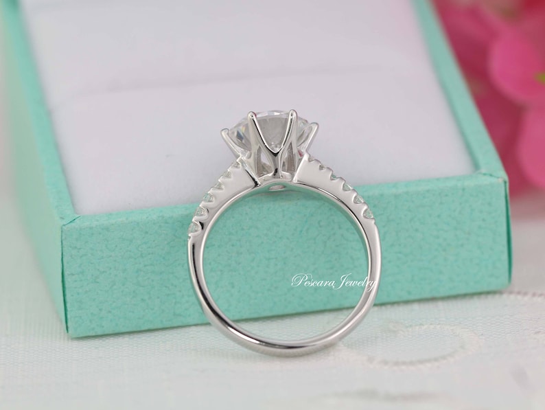 May include: A silver ring with a large, clear, round gemstone in the center. The ring has a band of smaller gemstones around the center stone.