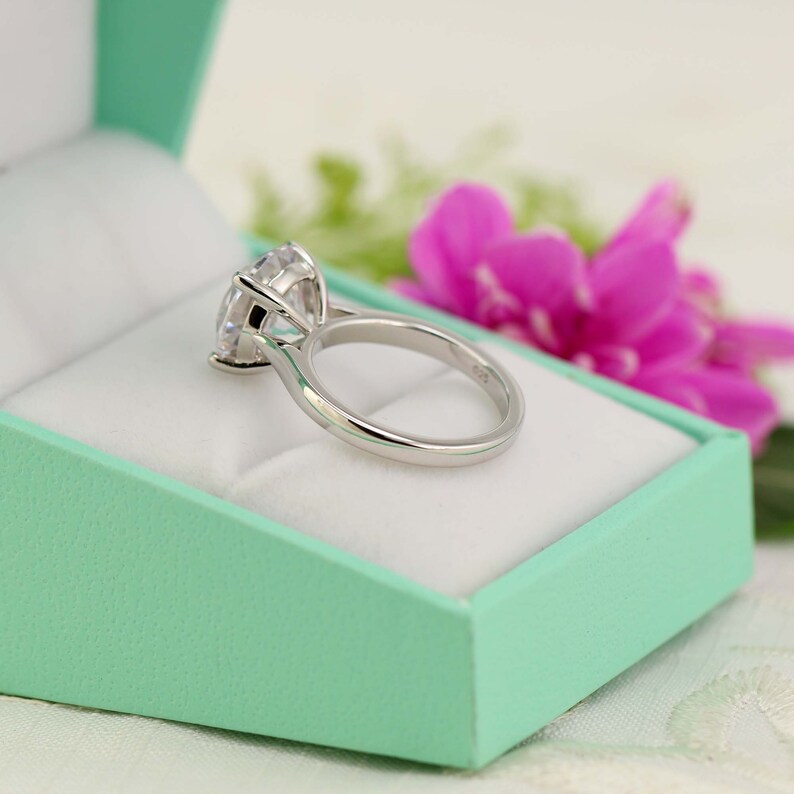 May include: A silver ring with a large, clear, round gemstone set in a prong setting. The ring is in a light green ring box.