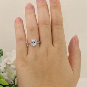 Op de afbeelding: Een zilveren ring met een ovale middelste steen die omringd is door kleinere stenen. De ring zit aan een vinger.