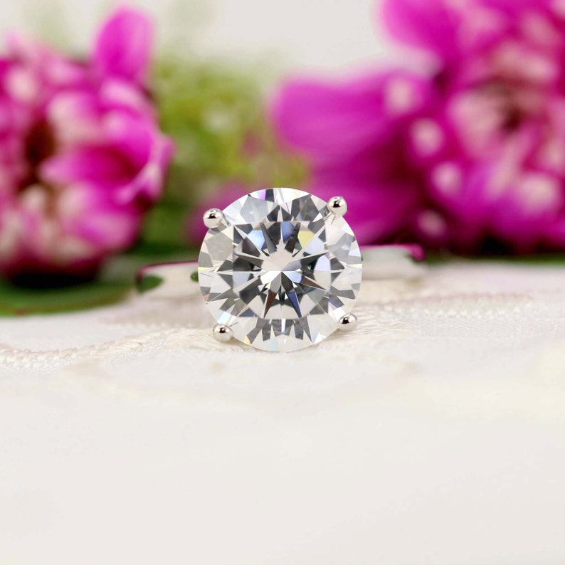 May include: A close-up of a silver ring with a large, round, clear diamond.