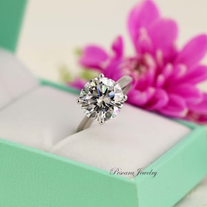 May include: A silver engagement ring with a large, round, clear diamond in a mint green ring box. The ring is set in a six-prong setting. The box has the words "Pescara Jewelry" printed on the front.