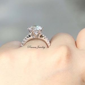 May include: A silver ring with a large, round, clear gemstone surrounded by smaller, clear gemstones. The ring is on a person's finger.