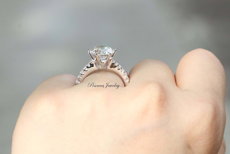 May include: A silver ring with a large, round, clear gemstone surrounded by smaller, clear gemstones. The ring is on a person's finger.