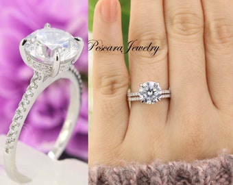 May include: A silver engagement ring with a large round center stone and a band of smaller stones. The ring is on a finger wearing a knitted sweater.