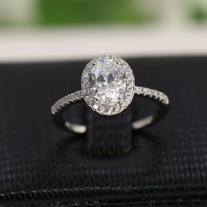 Op de afbeelding: Een zilveren ring met een ovale diamant in het midden, omringd door een halo van kleinere diamanten.