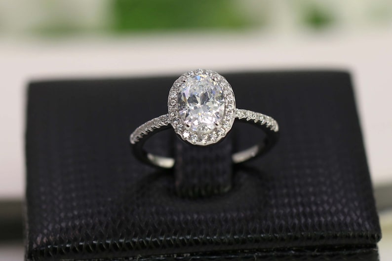 Op de afbeelding: Een zilveren ring met een ovale diamant in het midden, omringd door een halo van kleinere diamanten.
