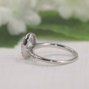Op de afbeelding: Een zilveren ring met een grote ovale, heldere steen omringd door kleinere heldere stenen.