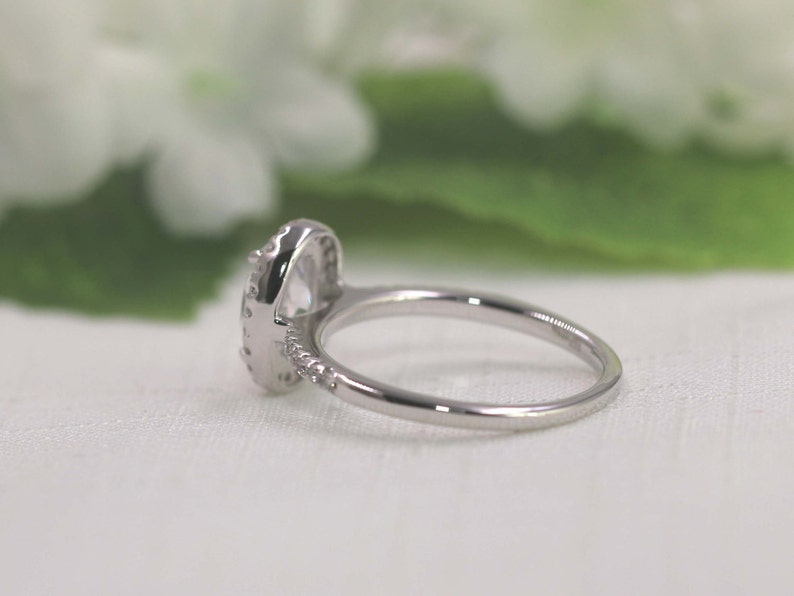 Op de afbeelding: Een zilveren ring met een grote ovale, heldere steen omringd door kleinere heldere stenen.