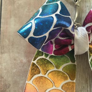 May include: A rainbow-colored bow with a mermaid scale pattern, attached to a silver key chain.