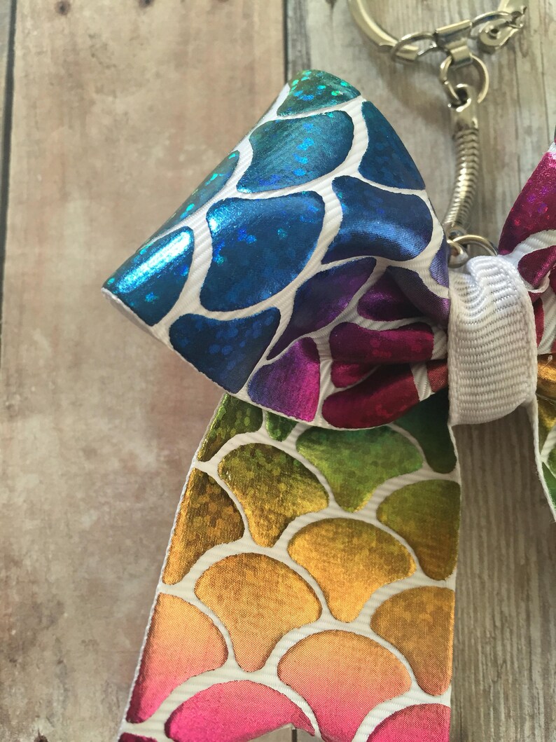 May include: A rainbow-colored bow with a mermaid scale pattern, attached to a silver key chain.