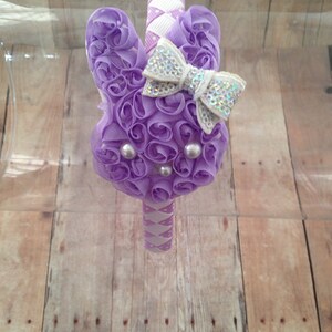 Puede incluir: Diadema morada y blanca con un gran lazo morado y un lazo blanco m&aacute;s peque&ntilde;o con purpurina plateada. La diadema est&aacute; decorada con peque&ntilde;as perlas blancas.