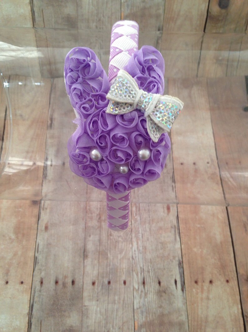 Puede incluir: Diadema morada y blanca con un gran lazo morado y un lazo blanco m&aacute;s peque&ntilde;o con purpurina plateada. La diadema est&aacute; decorada con peque&ntilde;as perlas blancas.