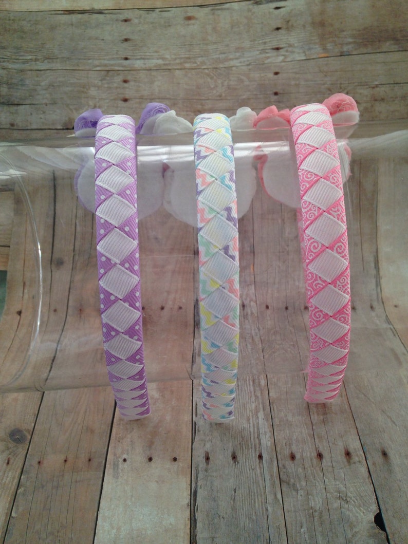 Puede incluir: Cuatro diademas coloridas con diferentes dise&ntilde;os de patrones. Las diademas est&aacute;n hechas de una cinta blanca y rosa con una base blanca y un patr&oacute;n rosa, morado o azul claro.