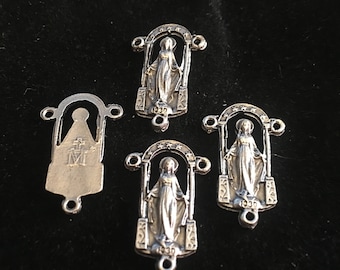 May include: Four silver-toned metal charms featuring the image of the Virgin Mary. Each charm has a different year inscribed on it: 1930, 1930, 1900, and 1900. One charm features the Virgin Mary with a cross and the letter M.