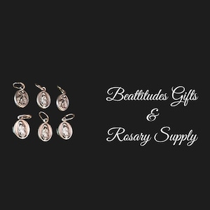 May include: Six silver charms featuring an image of the Virgin Mary. The charms are oval shaped and have a loop at the top for attaching to a chain or bracelet. The charms are arranged in two rows of three. The image is accompanied by the text "Beatitudes Gifts & Rosary Supply".