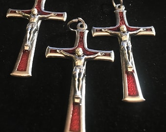 Op de afbeelding: Drie zilveren kruis hangers met rode emaille accenten. Elke hanger toont een afbeelding van Jezus Christus aan het kruis.