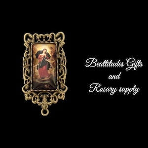 May include: A gold-toned metal frame with an ornate design surrounds a colorful image of the Virgin Mary, known as Our Lady of the Knots, holding a rope. The image is set against a cloudy sky. The text "Beatitudes Gifts and Rosary supply" is written in white cursive script below the frame.