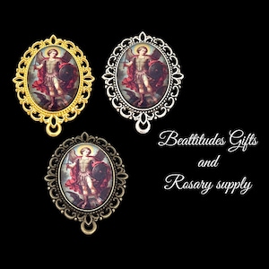 May include: Three oval pendants with ornate frames in gold, silver, and bronze. Each pendant features a religious image of a figure with a sword and shield. The text "Beattitudes Gifts and Rosary supply" is also visible.