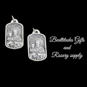 May include: Two silver pendants featuring a religious image of Saint Joseph holding the baby Jesus. The pendants are rectangular with a detailed design and a cross pattern.