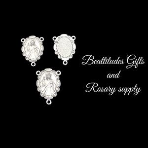 May include: Three silver-toned metal rosary centerpieces. Two feature an image of Jesus, and one is blank. The text "Beatitudes Gifts and Rosary supply" is visible in the background.