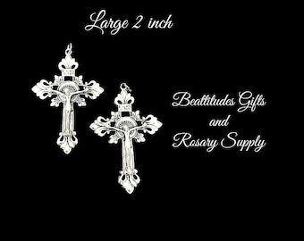 Op de afbeelding: Twee zilveren kruisbeelden met een gedetailleerd ontwerp, elk 5 cm lang. De kruisbeelden bevinden zich op een zwarte achtergrond met de tekst "Beattitudes Gifts and Rosary Supply" in wit.