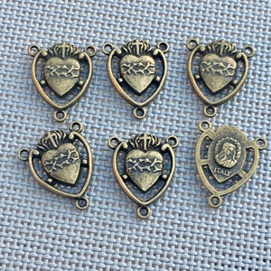 Puede incluir: Seis abalorios de metal dorado antiguo con un coraz&oacute;n con espinas y una cruz, y un abalorio con una representaci&oacute;n de la Virgen Mar&iacute;a y el texto "ITALIA".
