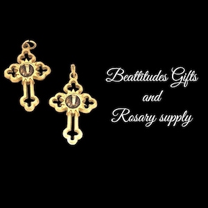 May include: Two gold-colored cross pendants with ornate designs and a central image. The crosses are displayed against a black background. The text "Beattitudes Gifts and Rosary supply" is also visible.