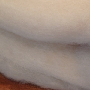 May include: A close-up of a pile of white wool roving. The wool is soft and fluffy, and it is perfect for felting or spinning.