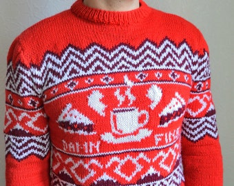 May include: Red knitted sweater with a white and purple geometric pattern. The sweater features a white mug with steam and a white pie on each side. The text "Drink in the Fire" is written in white below the mug.