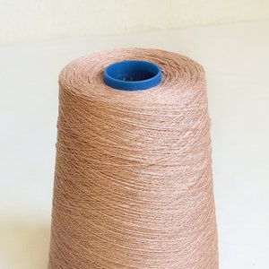 Puede incluir: Un cono de hilo de color marrón claro con un carrete de plástico azul.
