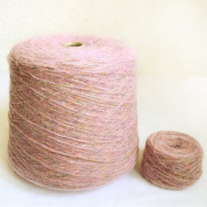 May include: Two spools of yarn. The larger spool is a light pink color with a cylindrical shape. The smaller spool is also light pink and round. Both spools have a soft, fuzzy texture and are suitable for knitting or crocheting projects.
