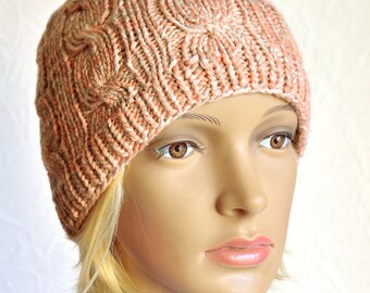 May include: A knitted beanie hat in a peach and cream color with a cable knit pattern.