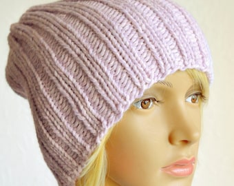 May include: A light pink knitted beanie hat with a ribbed texture. The hat is worn on a mannequin with blonde hair.