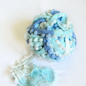 May include: A ball of blue, white, and light blue yarn with fuzzy pom-poms. The yarn is unraveling.
