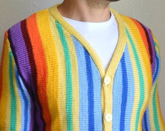May include: A striped cardigan with a rainbow color pattern. The cardigan has a yellow trim and buttons.