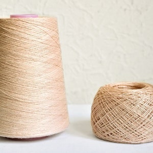 Può includere: Due bobine di filo beige, una è un cono pieno e l'altra è una palla più piccola.