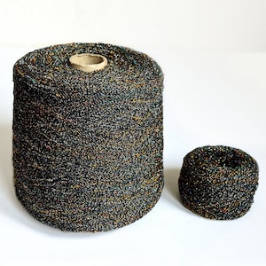 Może przedstawiać: Dwa szpulki czarnej przędzy z iryzującymi nitkami. Większa szpulka jest pełna, a mniejsza jest częściowo nawinięta.